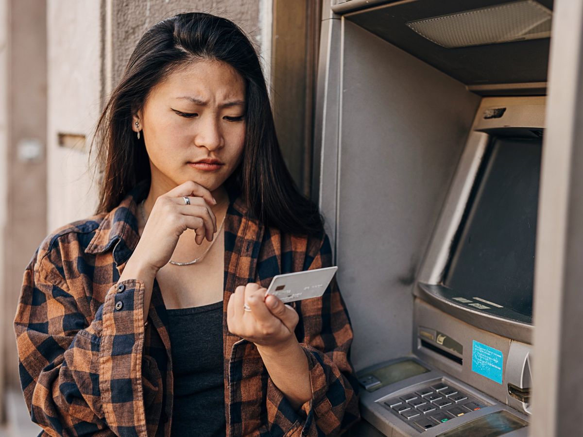 A woman at an ATM looking at her card, confused
