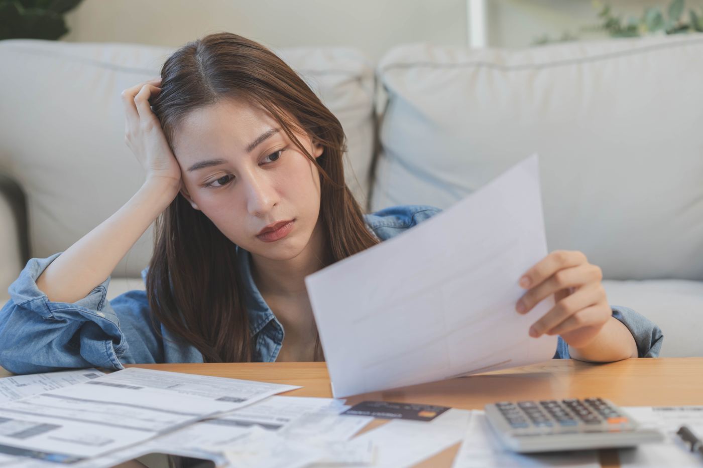Woman sitting by a sofa looking at a bank statement with a worried expression