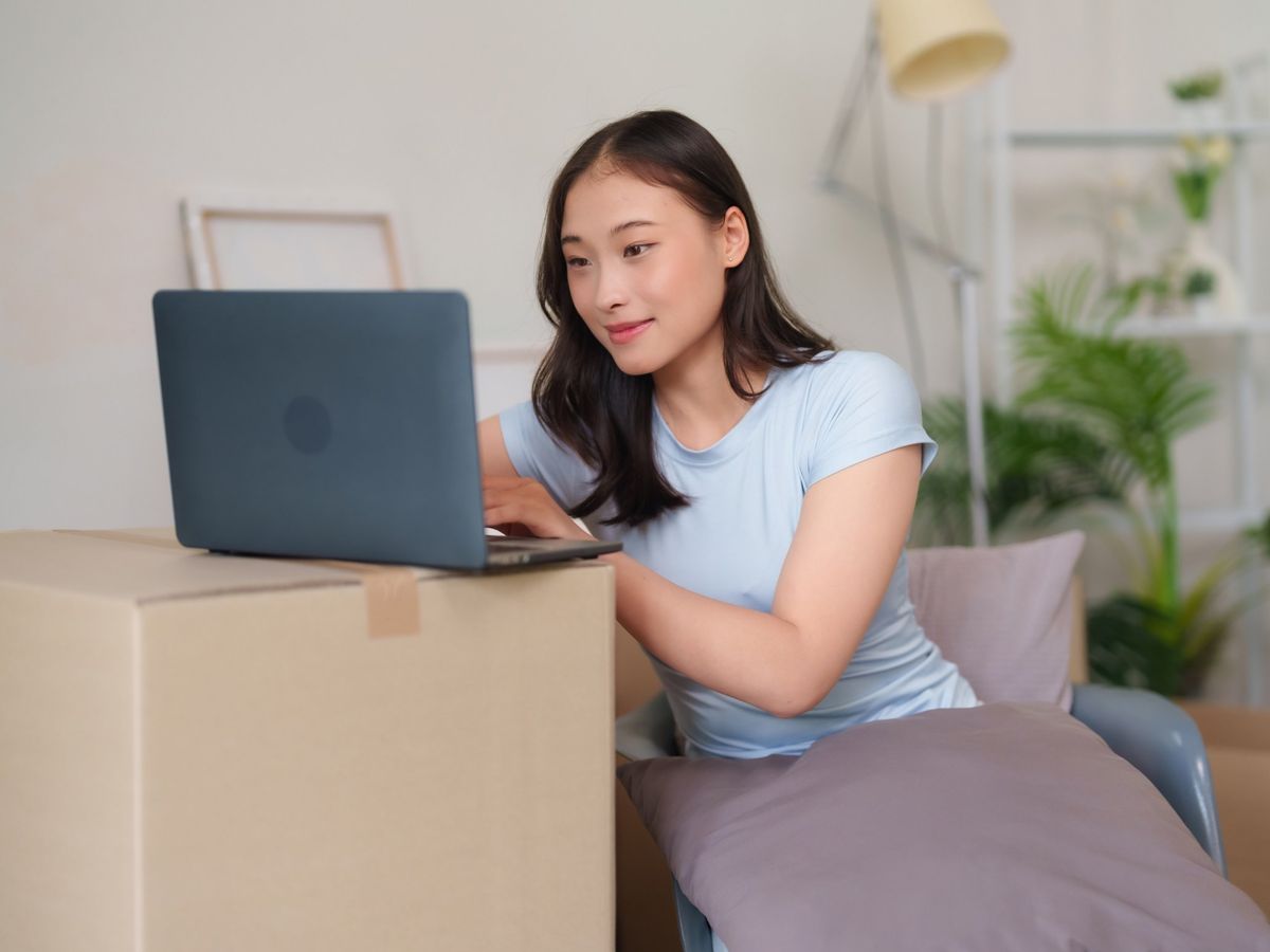 A woman in her new home using a laptop on a moving box, surrounded by boxes