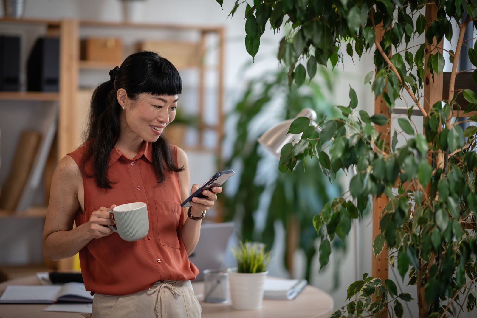 Woman at home holding a coffee, calmly checking her phone