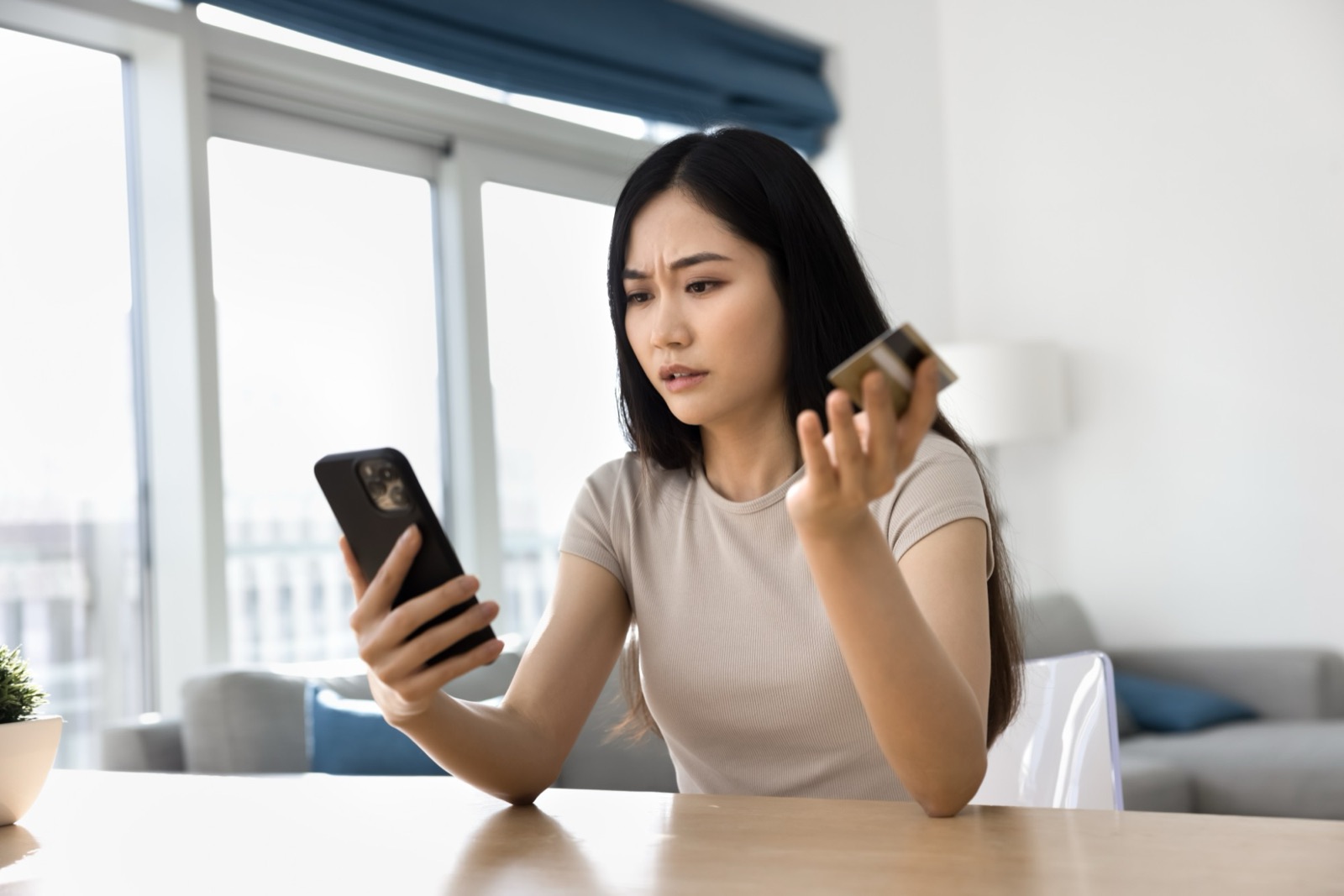 Woman looking puzzled at an unknown charge on her phone, holding a credit card